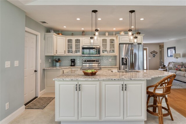 kitchen with an island with sink, decorative backsplash, appliances with stainless steel finishes, and glass insert cabinets