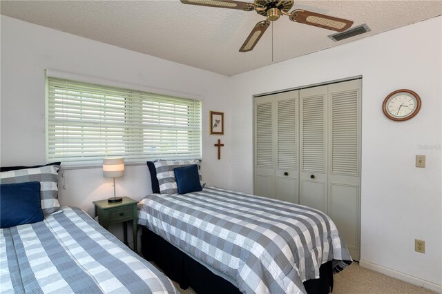 bedroom with visible vents, carpet floors, ceiling fan, a closet, and a textured ceiling