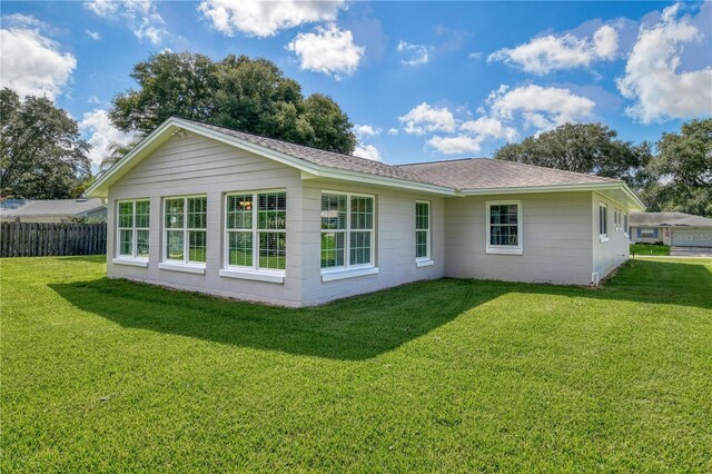 rear view of house featuring a lawn, fence, and a shingled roof