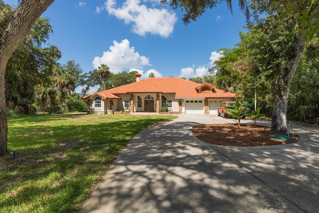 mediterranean / spanish-style home featuring a garage, a tile roof, driveway, a chimney, and a front yard