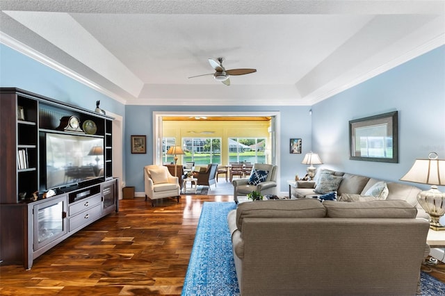 living room featuring ceiling fan, a raised ceiling, dark wood-type flooring, and crown molding