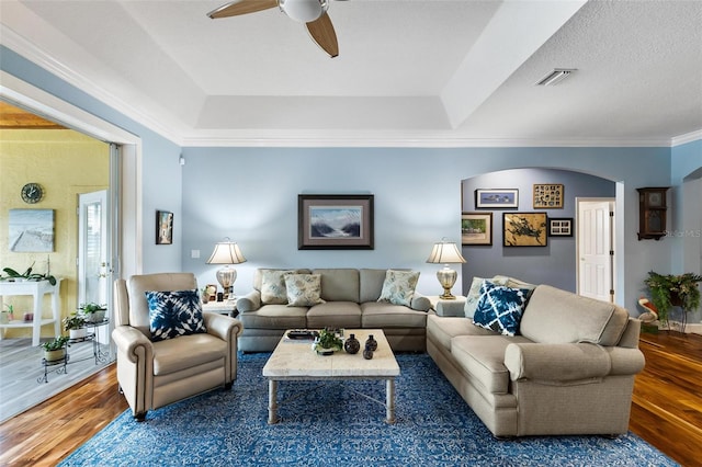 living room with ceiling fan, crown molding, wood-type flooring, and a raised ceiling