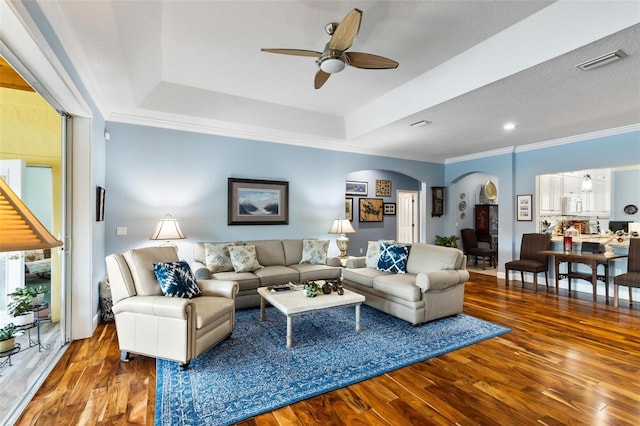 living room with ceiling fan, a raised ceiling, hardwood / wood-style flooring, and ornamental molding