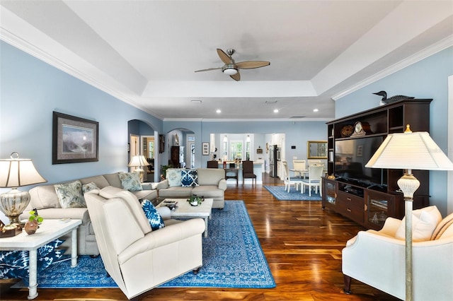 living room with ceiling fan, crown molding, dark wood-type flooring, and a tray ceiling