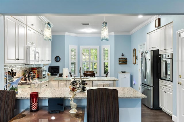 kitchen featuring dark hardwood / wood-style flooring, pendant lighting, stainless steel appliances, ornamental molding, and kitchen peninsula