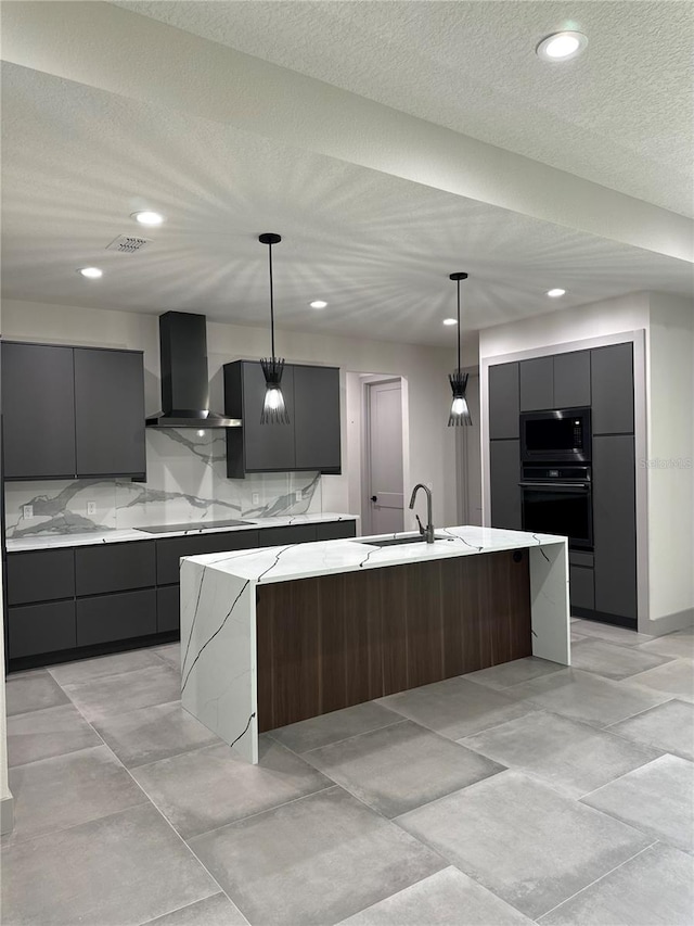 kitchen with wall chimney range hood, a large island, stainless steel microwave, sink, and decorative light fixtures