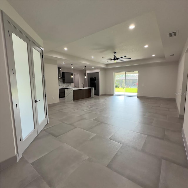 unfurnished living room with ceiling fan, french doors, a tray ceiling, and light tile patterned floors