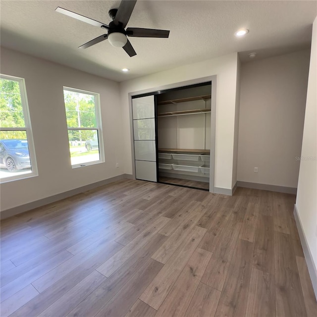 unfurnished bedroom featuring ceiling fan, hardwood / wood-style flooring, a closet, and multiple windows