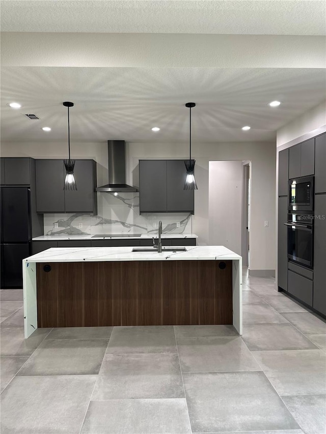 kitchen with sink, a kitchen island with sink, hanging light fixtures, wall chimney range hood, and black appliances