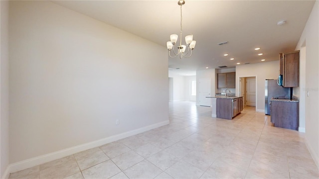 kitchen featuring an island with sink, sink, pendant lighting, an inviting chandelier, and light tile patterned floors