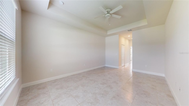 spare room with a healthy amount of sunlight, light tile patterned flooring, a raised ceiling, and ceiling fan