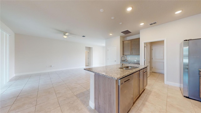 kitchen featuring a center island with sink, ceiling fan, appliances with stainless steel finishes, light stone countertops, and sink