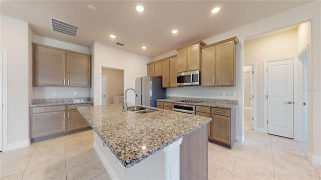 kitchen with a center island with sink, light tile patterned floors, stainless steel appliances, sink, and light stone counters