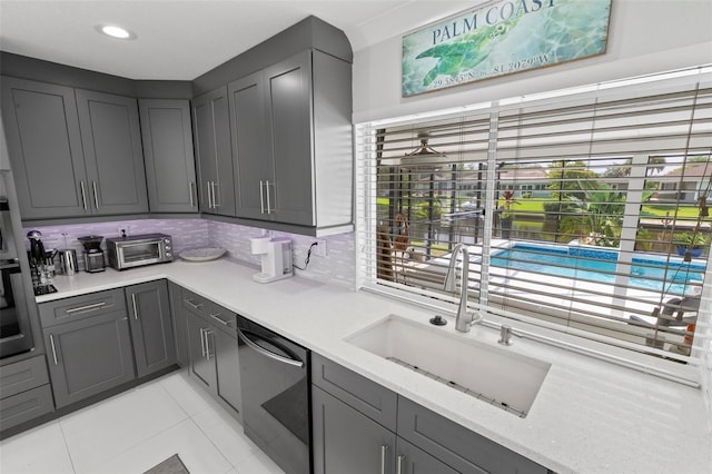 kitchen with light stone counters, light tile patterned flooring, a sink, backsplash, and dishwasher