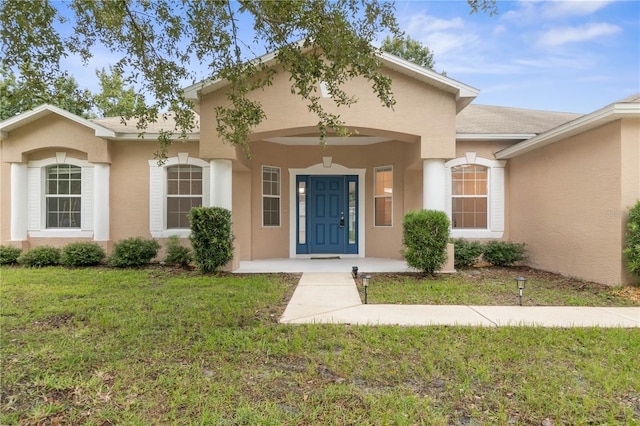 view of exterior entry with a lawn and stucco siding