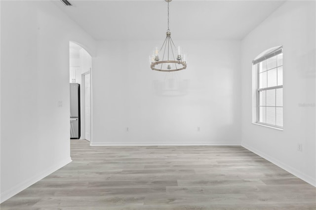 spare room with an inviting chandelier, light wood-style flooring, arched walkways, and baseboards