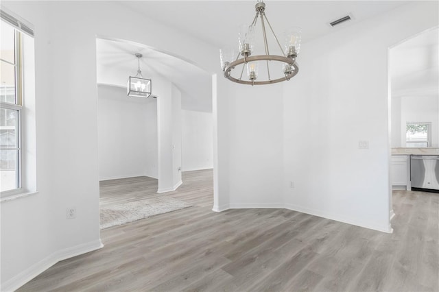 unfurnished dining area featuring arched walkways, visible vents, light wood-style flooring, a chandelier, and baseboards