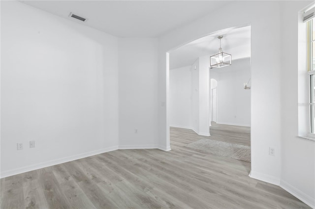 empty room featuring visible vents, arched walkways, baseboards, wood finished floors, and a notable chandelier