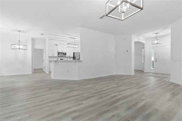 unfurnished living room with arched walkways, baseboards, a notable chandelier, and light wood finished floors