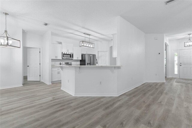 kitchen with light hardwood / wood-style flooring, stainless steel appliances, kitchen peninsula, pendant lighting, and white cabinets