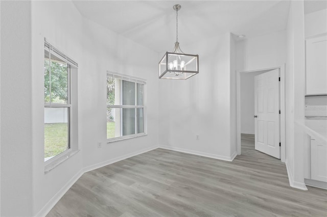 unfurnished dining area featuring a notable chandelier, light wood finished floors, and baseboards