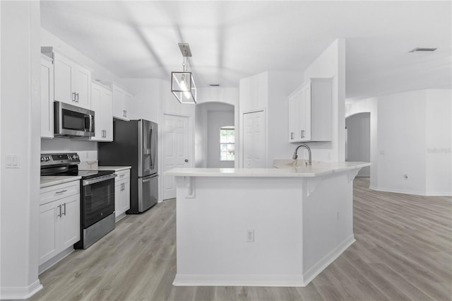 kitchen featuring arched walkways, a sink, white cabinets, light countertops, and appliances with stainless steel finishes