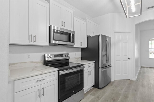 kitchen with stainless steel appliances, light hardwood / wood-style floors, white cabinetry, and light stone countertops