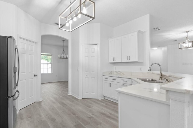 kitchen with light wood-type flooring, white cabinets, decorative light fixtures, kitchen peninsula, and stainless steel fridge