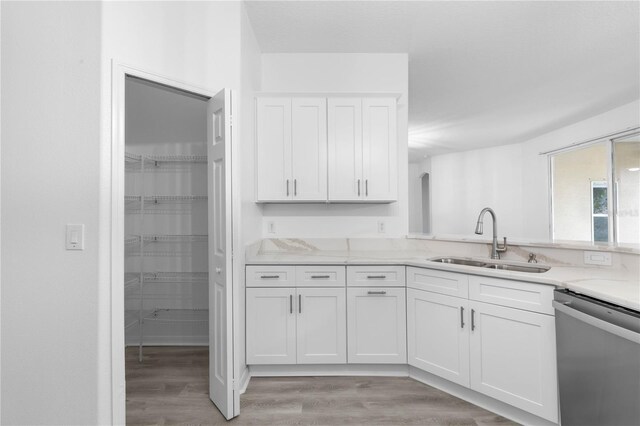 kitchen featuring light hardwood / wood-style floors, stainless steel dishwasher, sink, and white cabinetry