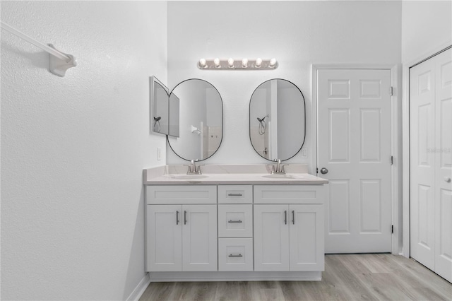 bathroom with double vanity, wood finished floors, a sink, and baseboards