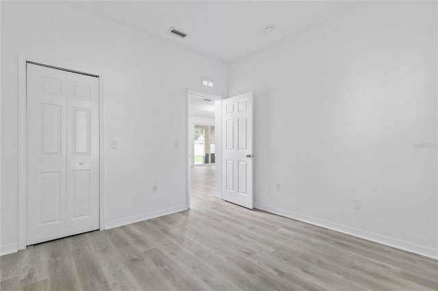 unfurnished bedroom featuring light wood-type flooring, a closet, visible vents, and baseboards