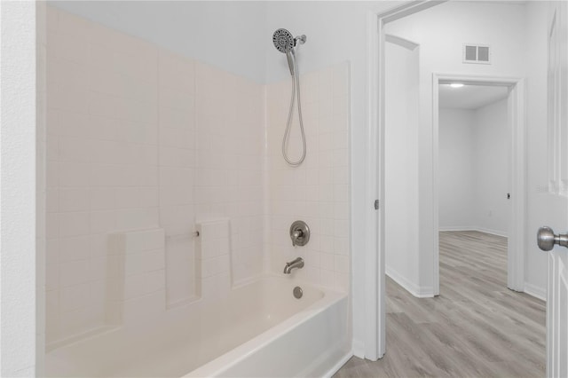 bathroom with washtub / shower combination, wood finished floors, visible vents, and baseboards