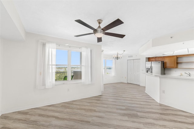 unfurnished living room with light wood-type flooring, a sink, and ceiling fan with notable chandelier