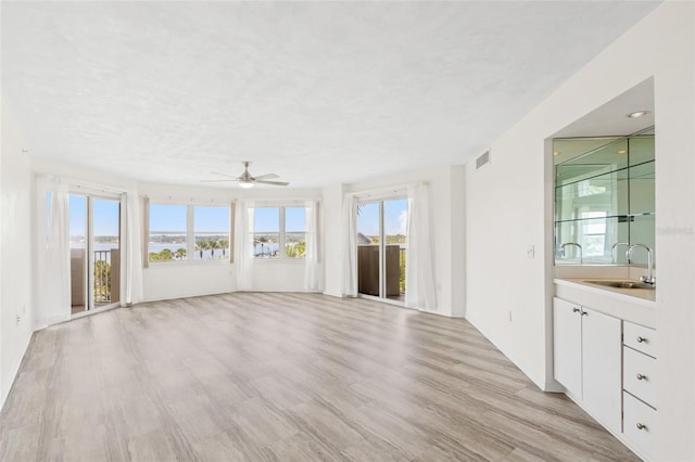 unfurnished living room with visible vents, light wood-style flooring, ceiling fan, a textured ceiling, and a sink