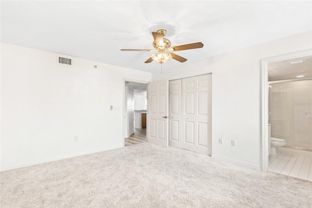 unfurnished bedroom featuring carpet floors, a closet, visible vents, a ceiling fan, and connected bathroom