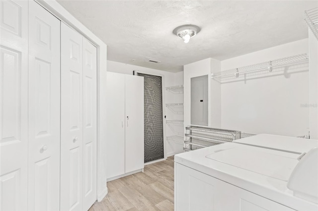 walk in closet with light wood-type flooring, electric panel, and washer and clothes dryer