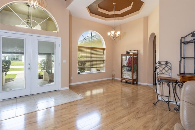 entryway with light wood-type flooring, a tray ceiling, a high ceiling, french doors, and an inviting chandelier