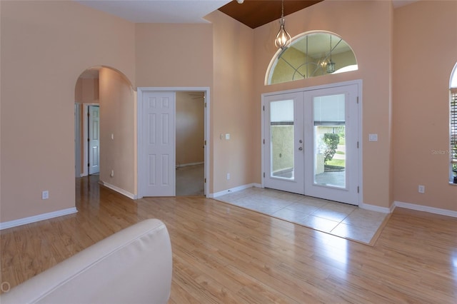 foyer entrance with arched walkways, a towering ceiling, wood finished floors, an inviting chandelier, and french doors