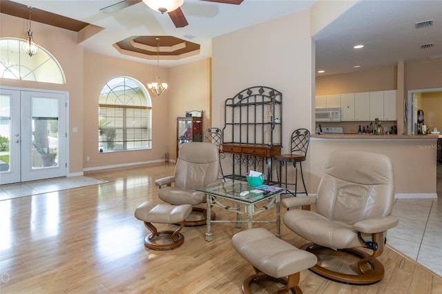 living area featuring ceiling fan with notable chandelier, wood finished floors, baseboards, french doors, and a raised ceiling