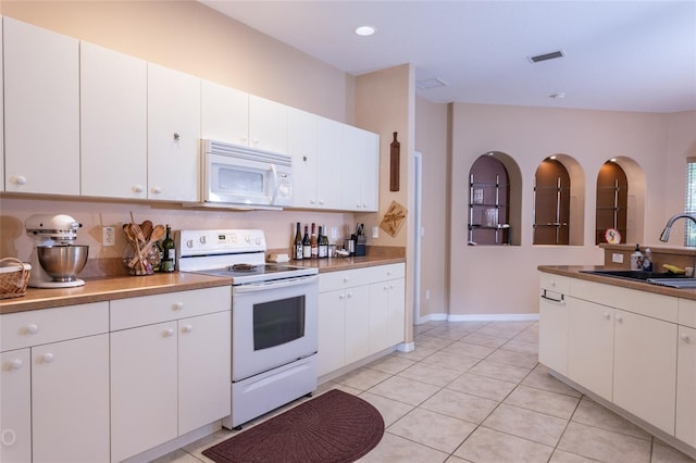 kitchen featuring white appliances, light tile patterned floors, visible vents, white cabinetry, and a sink