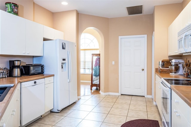 kitchen with white appliances, light tile patterned floors, visible vents, and arched walkways