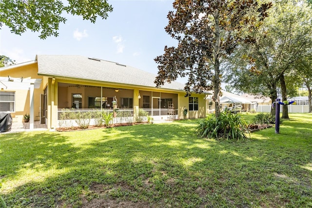 rear view of house featuring a lawn, fence, a sunroom, and stucco siding