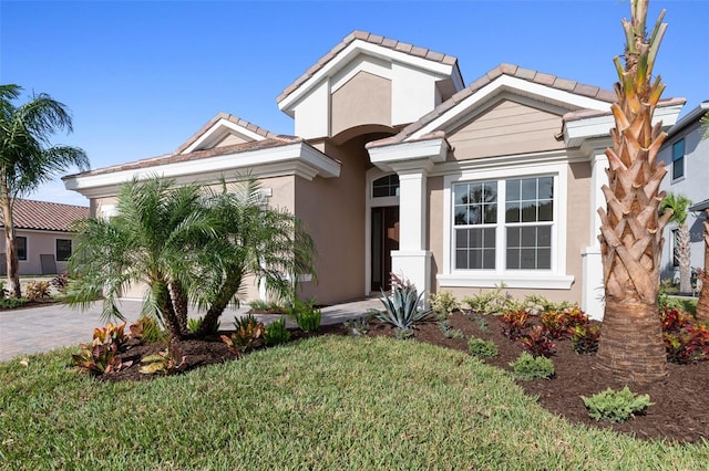 view of front of property with a tiled roof, a front yard, decorative driveway, and stucco siding