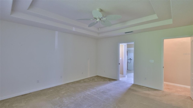 unfurnished room featuring light carpet, a tray ceiling, and ceiling fan