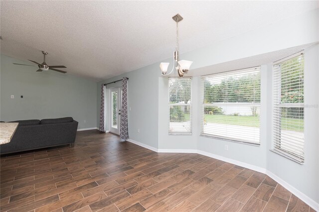 unfurnished dining area featuring lofted ceiling, wood tiled floor, a textured ceiling, baseboards, and ceiling fan with notable chandelier