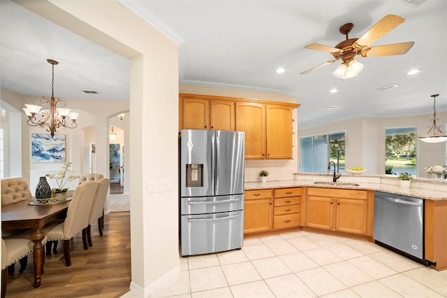 kitchen featuring sink, stainless steel appliances, light stone counters, pendant lighting, and ceiling fan with notable chandelier