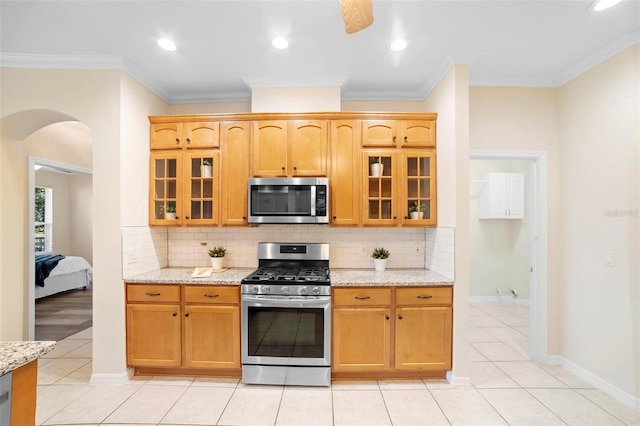 kitchen with light stone countertops, backsplash, stainless steel appliances, and ornamental molding