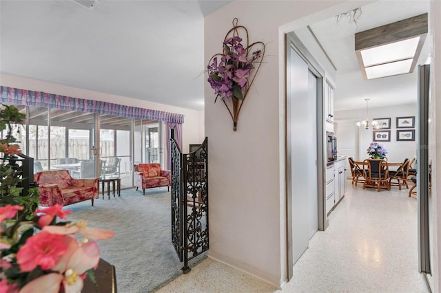 hall with baseboards, light speckled floor, and an inviting chandelier