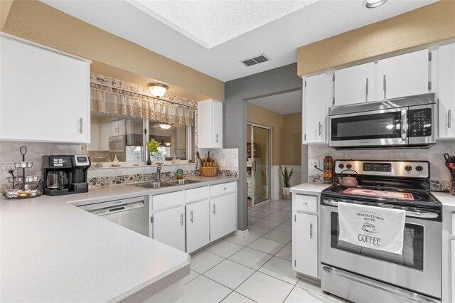 kitchen with backsplash, light tile patterned floors, sink, appliances with stainless steel finishes, and white cabinetry