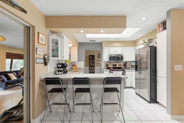 kitchen featuring a kitchen breakfast bar, tasteful backsplash, appliances with stainless steel finishes, kitchen peninsula, and light tile patterned flooring